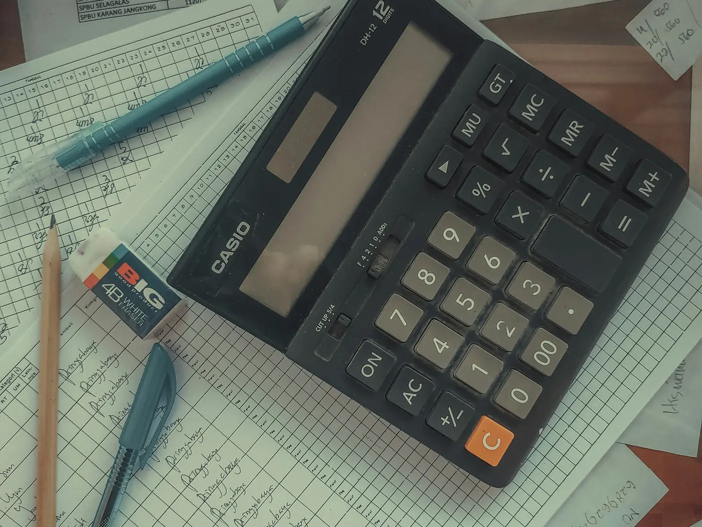 Calculatrice, registres et feuilles de saisie comptable posés sur un bureau
